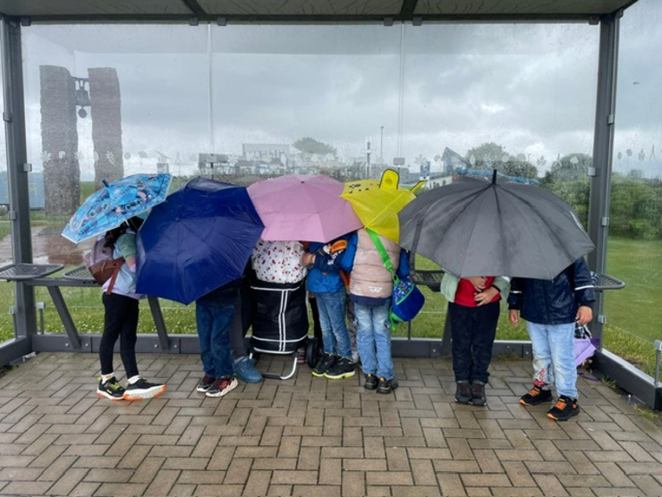 Kinder unter Regenschirme in Bushaltestelle